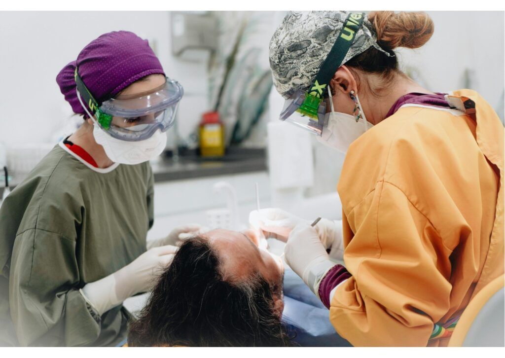 Dentists performing a dental implant procedure on a patient using protective gear and surgical tools in a clinical setting.