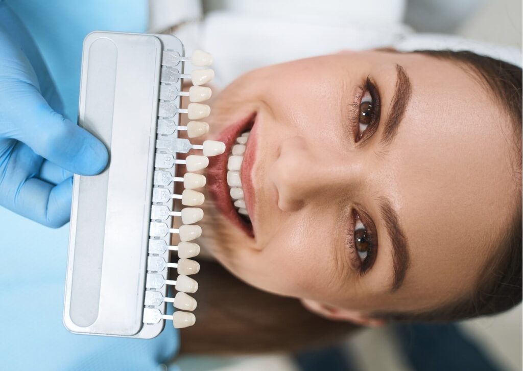 Patient comparing tooth shades during a cosmetic dentistry consultation to decide between dental bonding or porcelain veneers for a smile makeover.