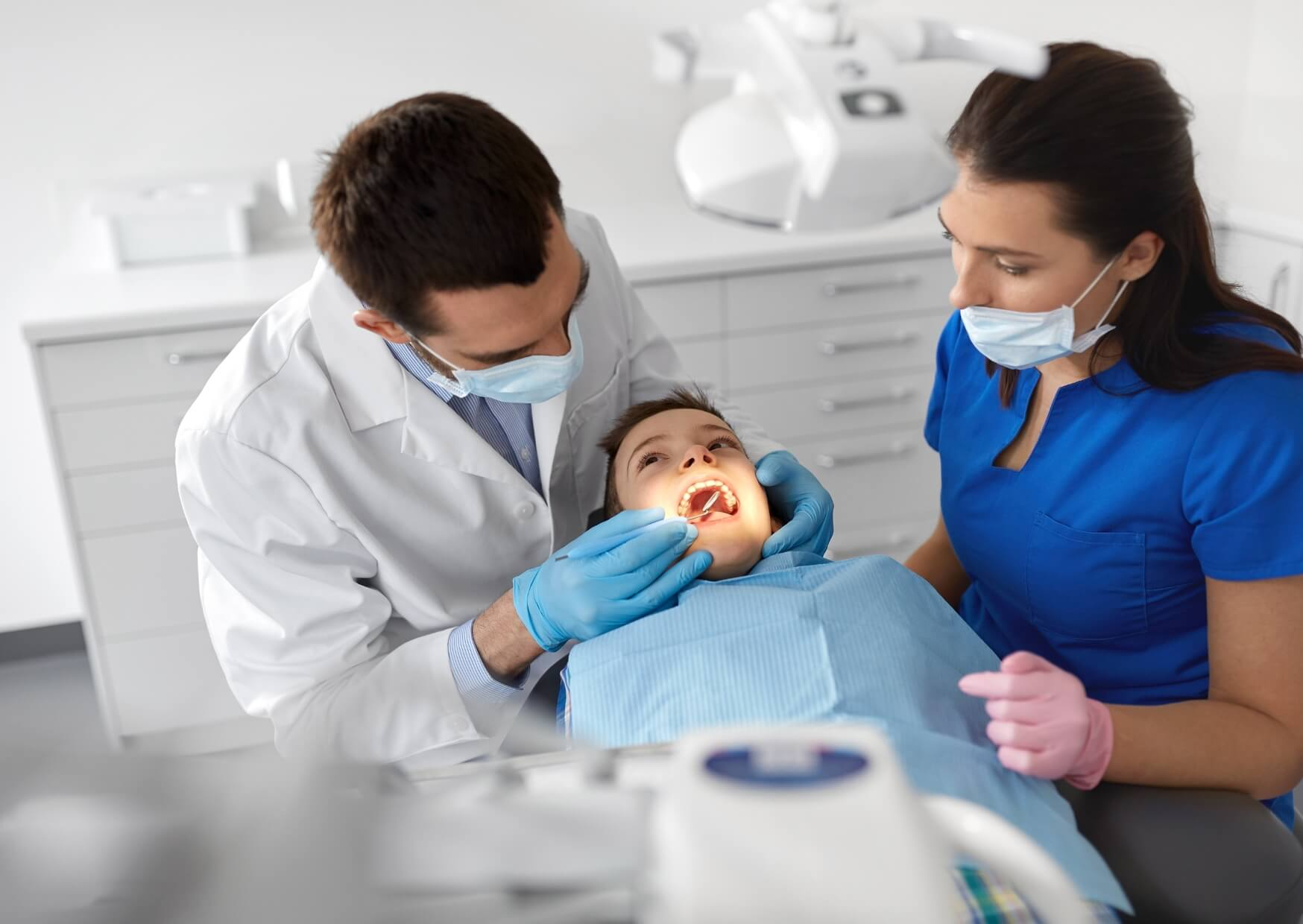 Pediatric dentist examining a young child's teeth during a routine dental visit to determine the right time for their first dental appointment.