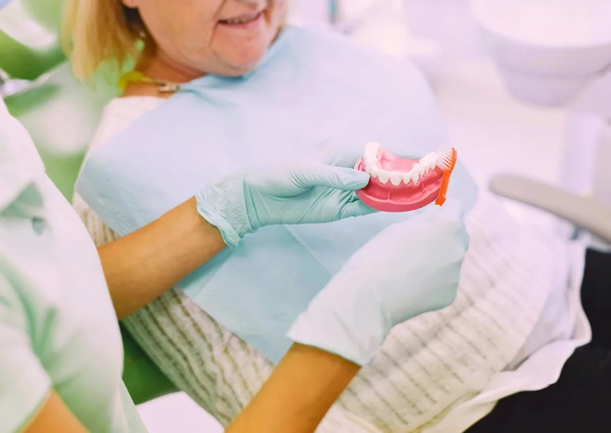 Dental professional demonstrating how to clean dentures with a toothbrush, emphasizing daily denture care to extend their lifespan.