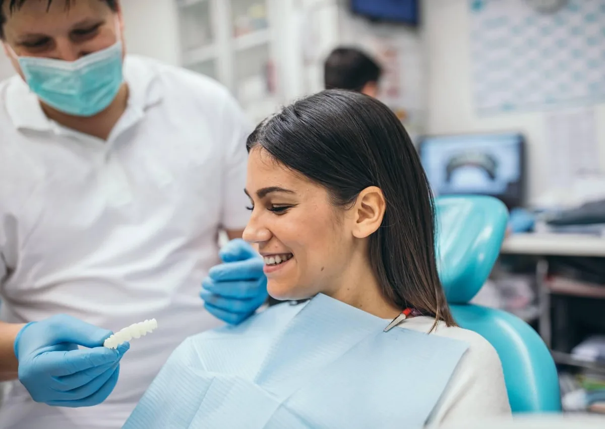 Dentist showing a patient a dental shade guide during a cosmetic dentistry consultation to discuss smile makeover options and expected results.